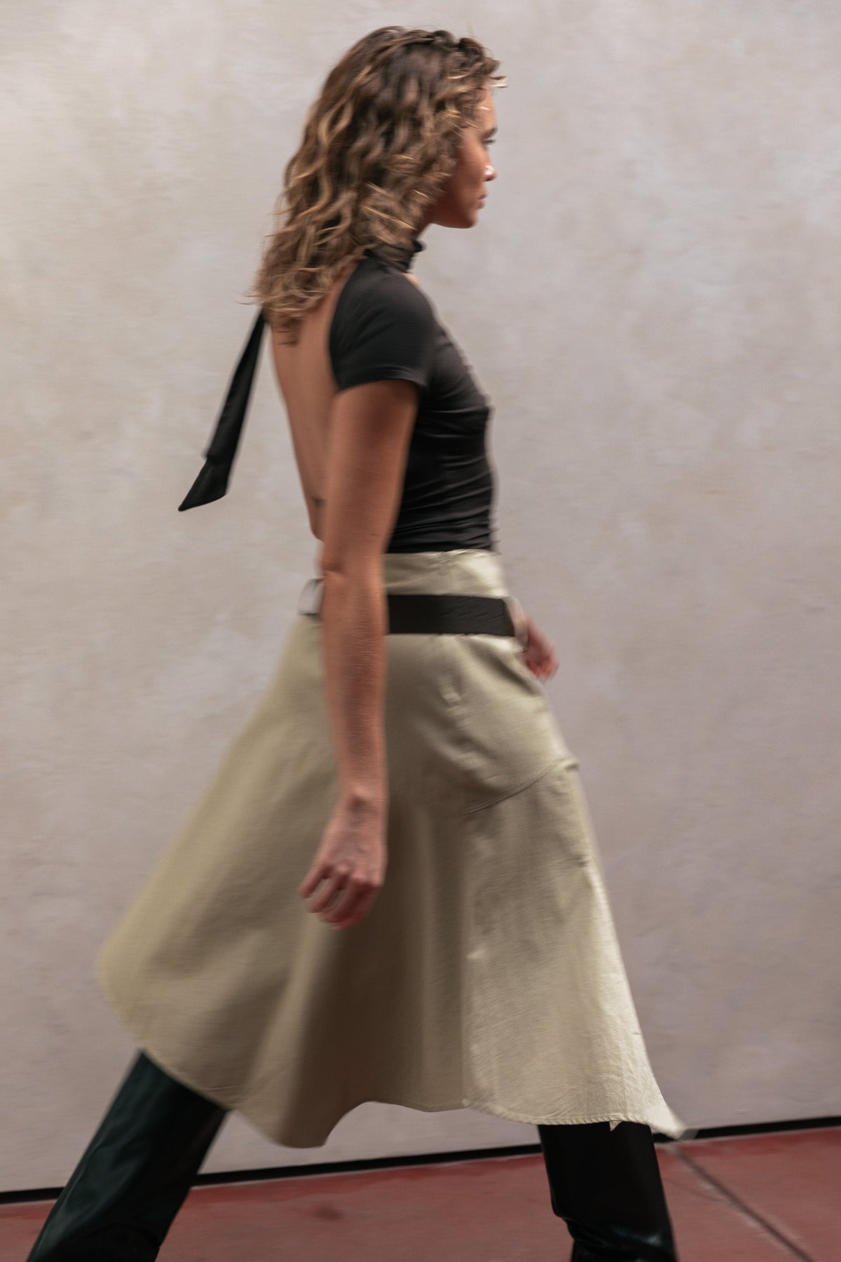 Woman wearing a black top and beige skirt against a plain background